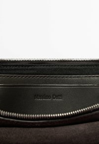Intérieur d'un sac en cuir noir avec fermeture éclair, présentant une doublure en tissu texturé et une étiquette embossée "Massimo Dutti".