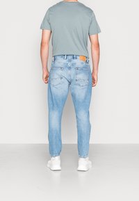 Jasnoniebieskie jeansy z denimu o zwężanym kroju, z pięcioma kieszeniami i brązową skórzaną naszywką z tyłu w talii; w połączeniu z szarą koszulką.