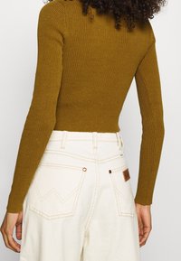 Ribbad långärmad topp i olivgrön, åtsittande siluett, matchad med vita högmidjade byxor med bakfickor och sömdetaljer.