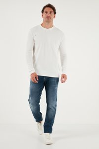 Weißes Langarm-Ripp-Shirt kombiniert mit ausgewaschenen dunkelblauen Jeans und weißen Sneakers, mit einer lässigen Passform und schlichtem Design.