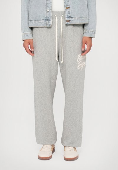 Graue Sweatpants aus weichem Stoff, mit lockerer Passform, verstellbarem Kordelzug und einem weißen Logo auf der linken Seite.