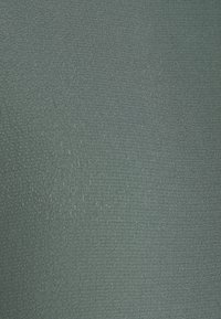 Gros plan sur un tissu vert clair texturé avec des motifs de tissage fins, irréguliers, horizontaux et verticaux.