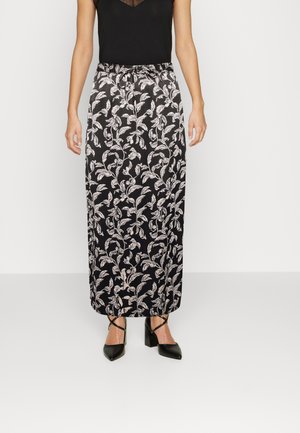 Saia maxi preta com um padrão de folhas brancas, cintura elástica e um design fluido. Combinada com uma blusa justa preta e sapatos de salto agudo.