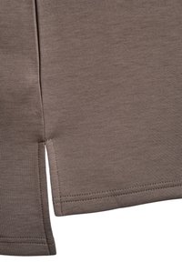 Gros plan sur un tissu marron avec un ourlet doublement surpiqué et une fente latérale sur un vêtement.