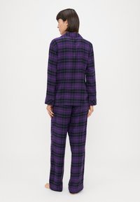 Μωβ καρό πιτζάμα με μακριά μανίκια και φαρδιές παντελόνες. Κατασκευασμένη από μαλακό ύφασμα, με μαύρες και ροζ λεπτομέρειες στο σχέδιο.