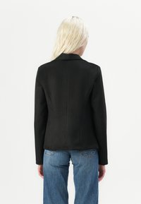 Svart tettsittende blazer med notched lapels, glatt tekstur og strukturert silhuett, parret med lyseblå brede bukser.