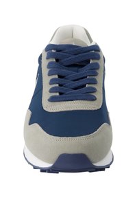 Zapatilla azul marino con acentos de ante gris, que presenta cordones planos, lengüeta acolchada y una suela de goma blanca. El tamaño y la forma indican un diseño atlético.
