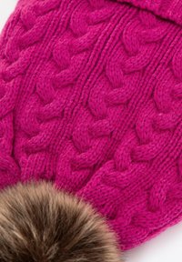 Różowa dzianinowa czapka z wzorem warkocza i dużym sztucznym pomponem z futra. Gruba i przytulna tekstura, idealna na zimne dni.