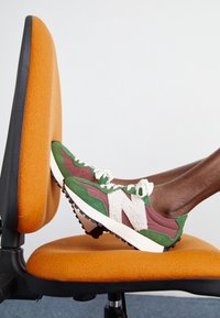 Zeleno-marošné tenisky s bílými akcenty a texturovanými materiály, vystavené na oranžové kancelářské židli.