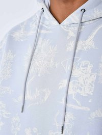 Felpa hoodie azzurro chiaro con stampa grafica bianca che presenta natura e figure. Include lacci con punte in metallo argentato e texture morbida.