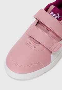 Chaussure en cuir rose avec des accents blancs, dotée d'une fermeture à bande auto-agrippante et d'une doublure en tissu texturé. Le logo Puma est visible sur la bande.