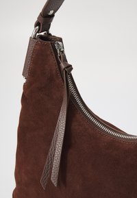 Braune Wildleder Schultertasche mit einem strukturierten Ledertrageriemen, ausgestattet mit einem silbernen Reißverschlussdetail und einer dekorativen Ledertassel.