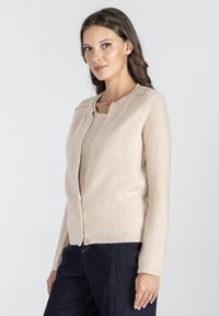 Beżowy sweter dzianinowy z okrągłym dekoltem i długimi rękawami, z zamkiem błyskawicznym z przodu oraz delikatnymi wypustkami na dole.