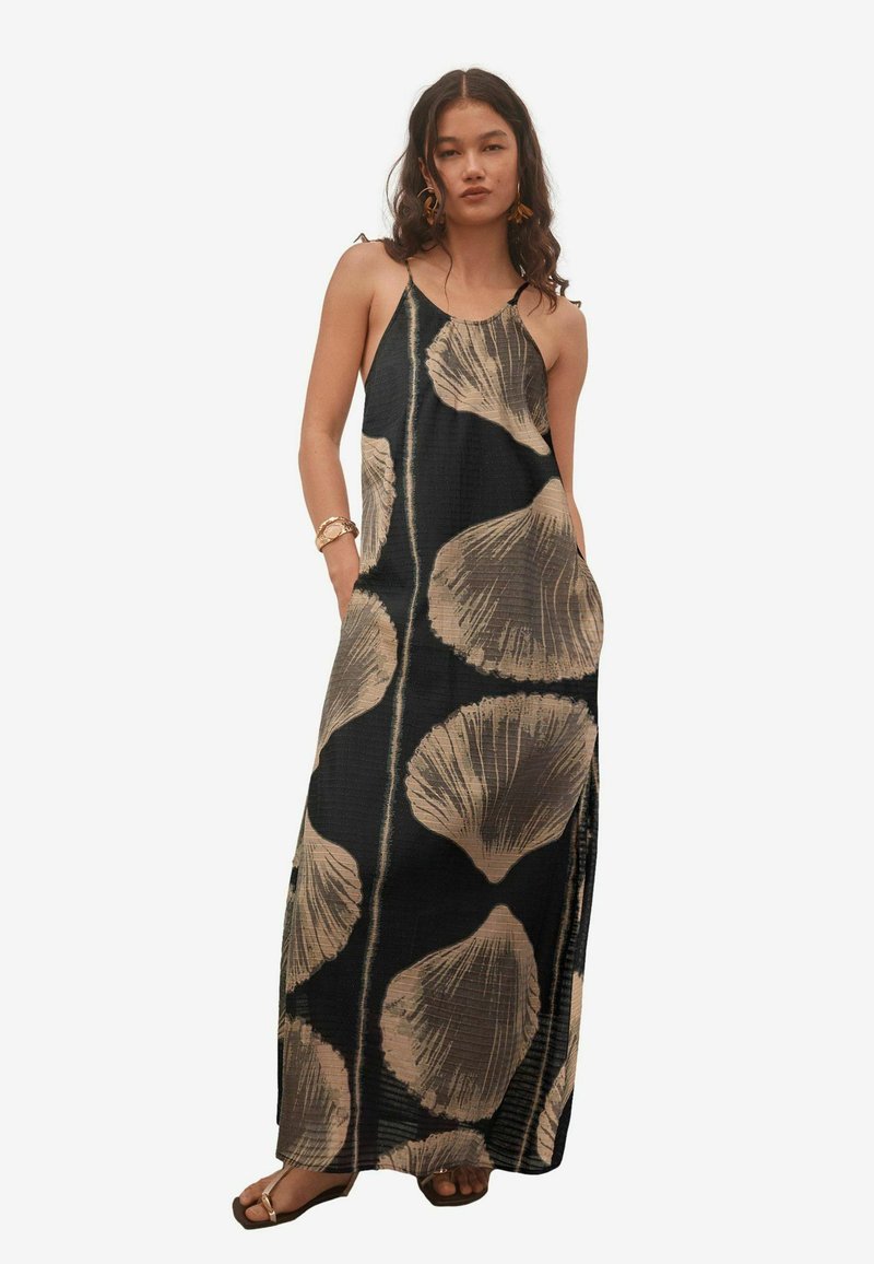 Robe maxi noire avec de grands motifs de coquillages beiges, dotée de fines bretelles, d'une coupe décontractée, de poches et d'une fente sur le côté pour faciliter les mouvements.