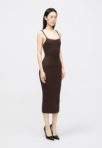 Καφέ ριγέ μίντι φόρεμα με φαρδιές τιράντες και διακοσμητική αλυσίδα στον λαιμό, σε συνδυασμό με μαύρες γόβες με μυτερή μύτη.