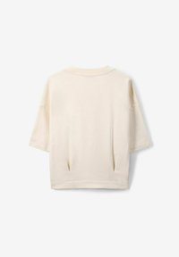 Haut à manches courtes de couleur crème fabriqué en tissu doux. Présente un col rond, des fentes latérales et une coupe décontractée avec des coutures minimales.