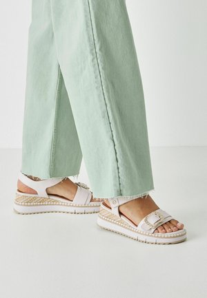 Sandales à plateforme blanches avec une texture tissée et de larges lanières, associées à un pantalon vert menthe à jambes larges avec des bords effilochés.