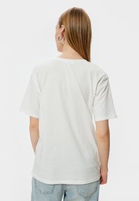 Hvid bomulds T-shirt med korte ærmer og en afslappet pasform. Rund hals, glat overflade og et enkelt design. Bæres med lyseblå jeans.