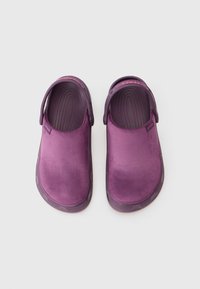 Egy pár lila Crocs klumpa zárt, velúrszerű felsőrésszel és állítható sarokpántokkal, fehér háttér előtt.