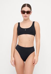 Black bikini set featuring a cropped top with a logo on the front and high-waisted bottoms. Smooth texture and minimal design.
