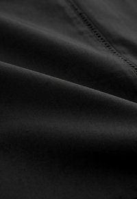 Tissu noir à la texture lisse, présentant un subtil éclat et un délicat bord décoratif. Le matériau semble léger et flexible.
