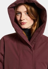 Burgundy huppari, jossa on sileä pinta ja jämäkkä muotoilu; siinä on korkea kaulus ja näkyvissä ompeluyksityiskohdat.