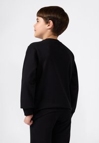 Felpa nera in cotone con maniche lunghe e colletto rotondo, con una texture liscia e una vestibilità comoda indossata da un bambino.