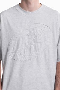 Lys grå bomulds T-shirt med et struktureret, præget logo design i midten. Korte ærmer og en rund halsudskæring. Blødt, afslappet stof.