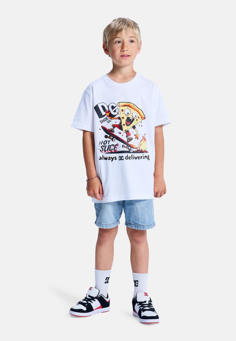 Ein weißes Baumwoll-T-Shirt mit einem bunten Grafikdesign eines Cartoon-Pizzastücks auf einem Skateboard. Kombiniert mit Jeansshorts und schwarzen Sneakers.