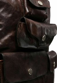 Mochila de cuero marrón con múltiples bolsillos exteriores con cierres a presión, superficie texturizada y detalles de costura visibles.