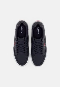 Ténis de desporto pretos com um cabedal têxtil liso, sola de borracha branca e atacadores tonais. Apresenta a marca Levi's na língua e na lateral.