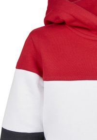 Felpa con cappuccio rossa e bianca caratterizzata da un design bicolore con una texture morbida. Include un cappuccio e una sezione inferiore di colore grigio scuro a contrasto.