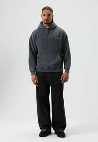 Sweat à capuche en polaire gris charbon avec poche avant, poignets côtelés et capuche à cordon, associé à un pantalon noir à jambes larges et des chaussures noires épaisses.