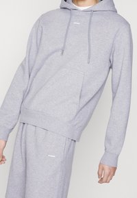 Sudadera gris hecha de un tejido suave, con un bolsillo frontal tipo canguro, cordones y puños acanalados, combinada con pantalones cortos a juego.