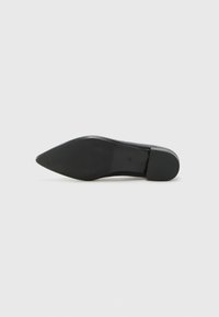 Chaussure noire à bout pointu avec une texture en cuir lisse et un petit talon rond. La semelle extérieure est plate et texturée pour une meilleure adhérence.
