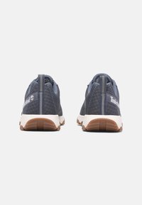 Námořnické modré sportovní boty s texturovanou tkaninou, bílou mezipodešví a podešví z gumy. Obsahují logo Timberland a poutko na zadní straně.