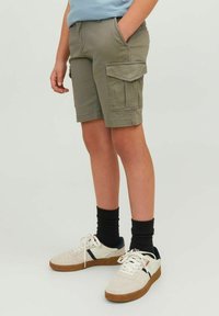 Pantaloni cargo color kaki con più tasche, passanti per cintura e taglio dritto. Indossati con sneakers bianche e calzini neri.