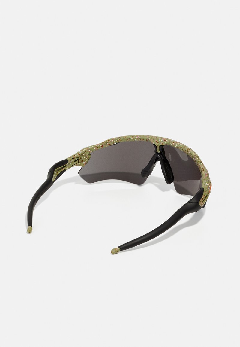 Sonnenbrille mit einem grün gesprenkelten Rahmen, schwarzen Bügeln und dunklen Gläsern. Merkmale sind strukturierte Akzente und ein geschwungenes Design.