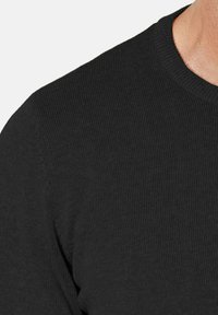 Suéter negro de punto acanalado con cuello redondo, textura suave y forma ajustada. Costuras visibles a lo largo de la costura del hombro.