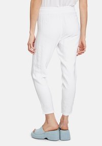 Bílé, lehké kalhoty s elastickým pasem, splývavým střihem a texturovaným materiálem, doplněné světlemodrými platformovými sandály.