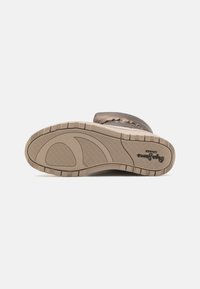 Kautrābe ar teksturētu virsmu bēšā krāsā, kurā ir izcilas formas un rievas saķerei. Zīmola nosaukums ir redzams uz sāniem.