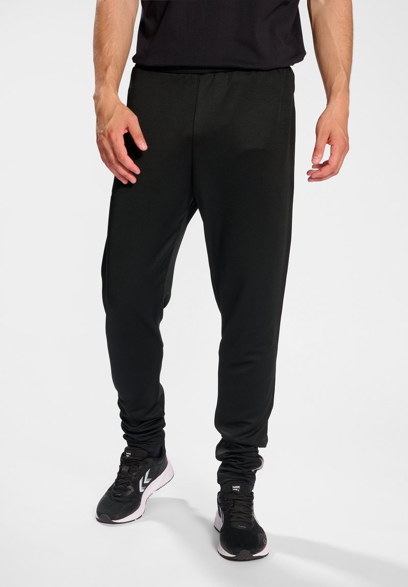 Schwarze sportliche Jogginghosen mit einem elastischen Bund, schmal zulaufenden Beinen und glattem Stoff; kombiniert mit schwarzen Laufschuhen mit weißen Akzenten.