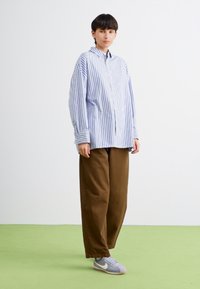 Blå og hvite stripete oversized skjorte med knappeåpning, parret med brune vidde bukser og grå sneakers. Mykt, uformelt stoff.