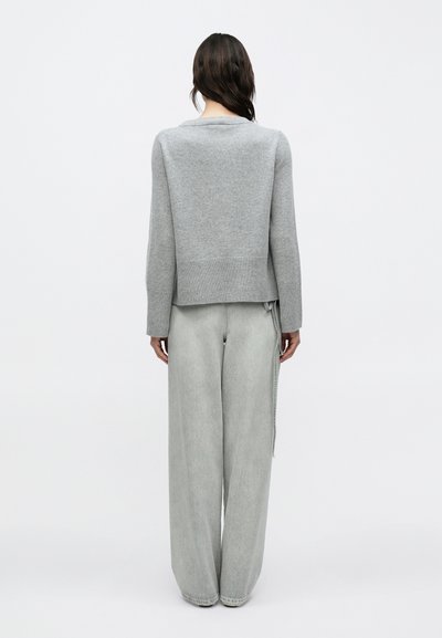 Γκρι πλεκτό πουλόβερ με στρογγυλή λαιμόκοψη και ριμπ τελείωμα, συνδυασμένο με ανοιχτό γκρι τζιν παντελόνι φαρδύ στο τελείωμα με λεπτομέρεια πλαϊνής ραφής.