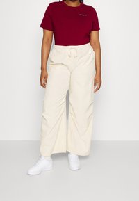 T-shirt in cotone borgogna a maniche corte con un piccolo logo; pantaloni cargo ampi color crema con coulisse; abbinati a sneakers bianche.