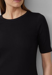 Svart ribbad kortärmad topp med rund halsringning. Tyget har en slät yta med vertikala linjer och subtila sömnadsdetaljer.
