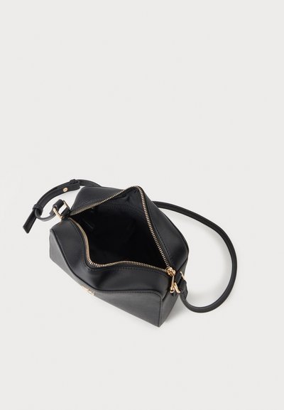 Sac bandoulière en cuir noir avec fermeture éclair dorée partiellement ouverte, montrant l’intérieur vide et la sangle réglable sur fond blanc.