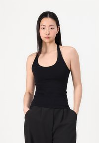 Top negru fără mâneci, cu un design ajustat și decolteu rotunjit. Fabricat dintr-un material neted și elastic, asortat cu pantaloni negri cu talie înaltă.