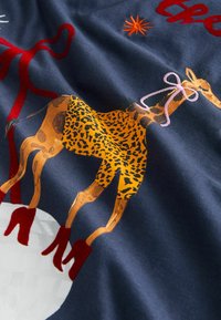 Navy fabric featuring a patterned giraffe with orange and black spots, red high heels, and decorative embroidery. Accents include a pink bow.