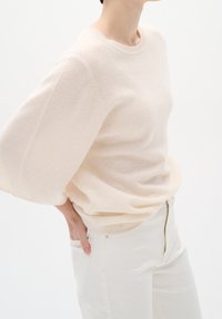 Jersey beige claro con cuello redondo, mangas cortas holgadas y textura de punto suave, combinado con pantalones ajustados de color claro.